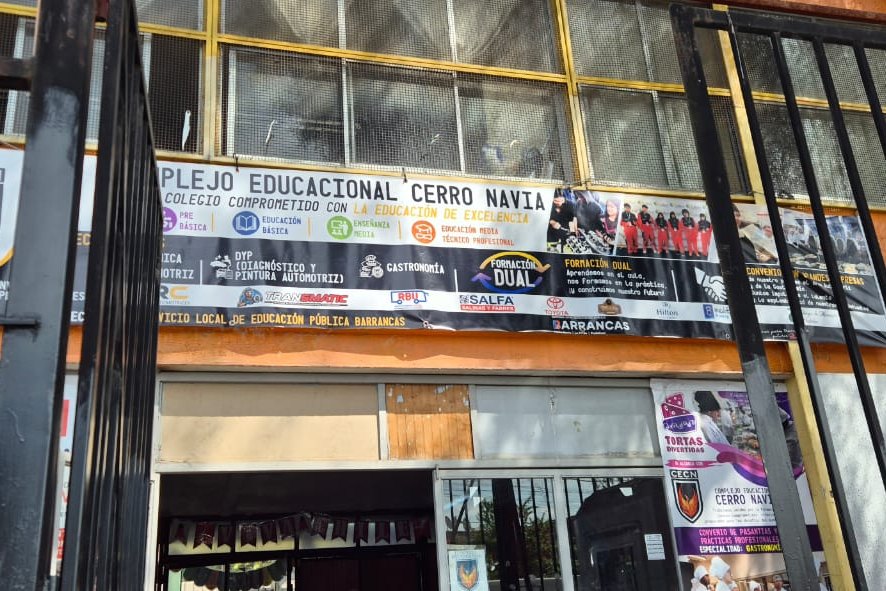 Fachada del Complejo Educacional Cerro Navia vista entre las rejas de la entrada, con un lienzo que anuncia sus niveles y especialidades.