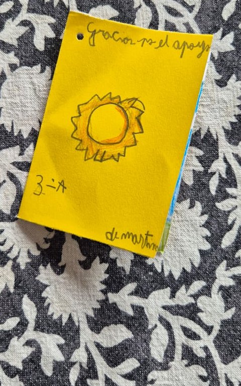 Tapa de una tarjeta amarilla hecha a mano, con un sol dibujado con lápices de colores y la dedicatoria «Gracias por el apoyo», 3.º A.
